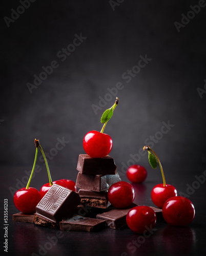 Pieces of dark chocolate and fresh cherry on a dark background. Copy space