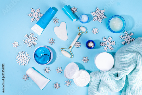 Winter skin care and hand care cosmetic in unbranded containers, bottles, tubes with artificial snowflakes on light blue background. Winter hand skin care cosmetics background top view copy space 