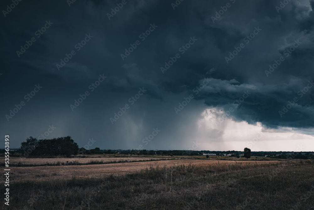 A huge storm cloud with a wall of rain in the countryside.