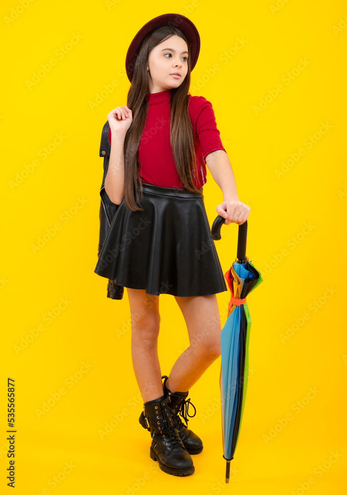 Fashion autumn kids weather. Child teenager girl with rainbow umbrella in autumn black leather skirt boots and hat isolated on yellow studio background. Autumn kids trendy clothes fall season Fashion autumn kids weather. Child teenager girl with rainbow umbrella in autumn black leather skirt boots and hat isolated on yellow studio background. Autumn kids trendy clothes fall season