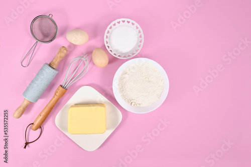 Cake dough ingredients and baking tools on pink background with copy space