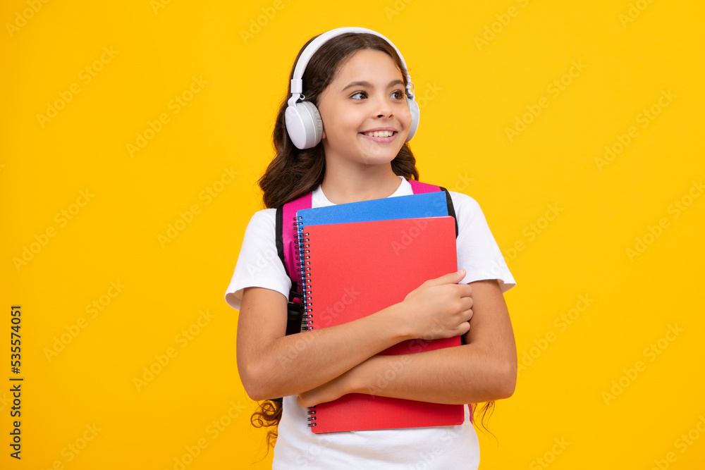 Schoolgirl, teenage student lifestyle girl in headphones hold books on yellow isolated studio background. School and music education concept. Schoolgirl, teenage student lifestyle girl in headphones hold books on yellow isolated studio background. School and music education concept.