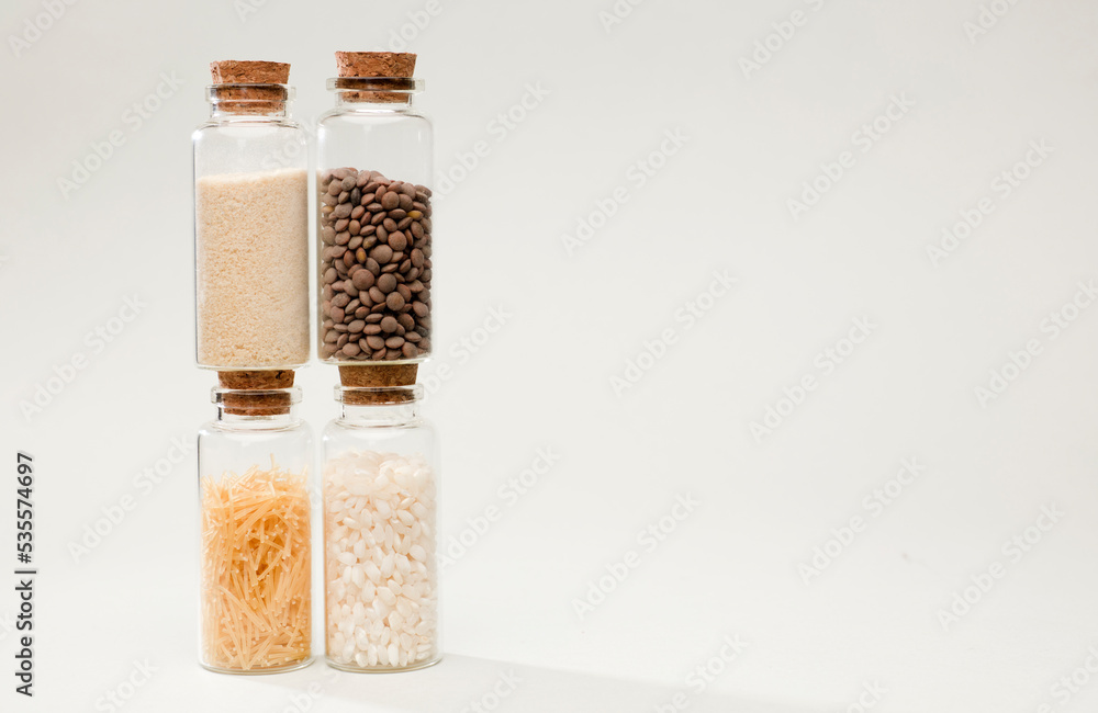 four glass jars with cork stopper, bread, lentils, pasta and rice, soft greenish background four glass jars with cork stopper, bread, lentils, pasta and rice, soft greenish background