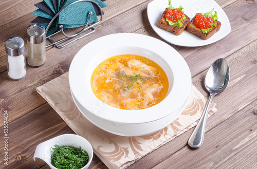 Fish soup - Russian fish soup with sandwiches with red caviar in a plate on a dark wooden background.