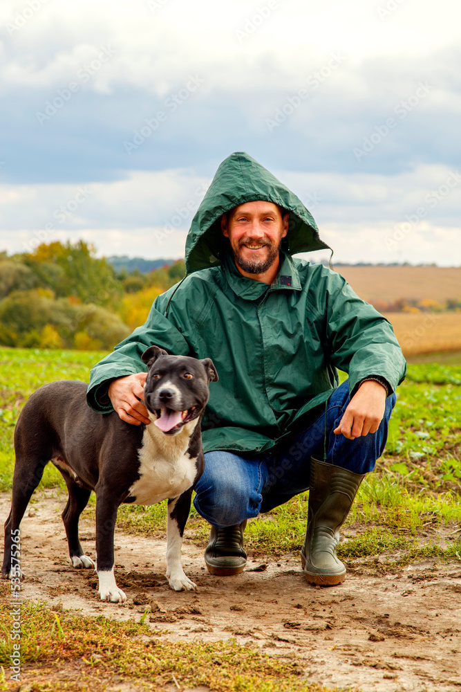 A man walks his dog in a field after a thunderstorm. Guy with staffordshire terrier in nature on a cloudy day. The concept of freedom, happiness, friendship, nature. A man walks his dog in a field after a thunderstorm. Guy with staffordshire terrier in nature on a cloudy day. The concept of freedom, happiness, friendship, nature.