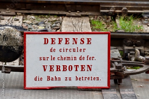 Historic safety sign on railway tracks saying in French and German 'FORBIDDEN walking on railway tracks'