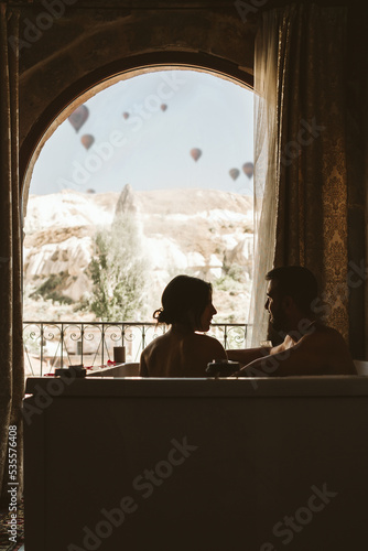 Couple taking a bath in the hotel in front of a window with hot air balloons flying in the background of the landscape - Cappadocia  Turkey