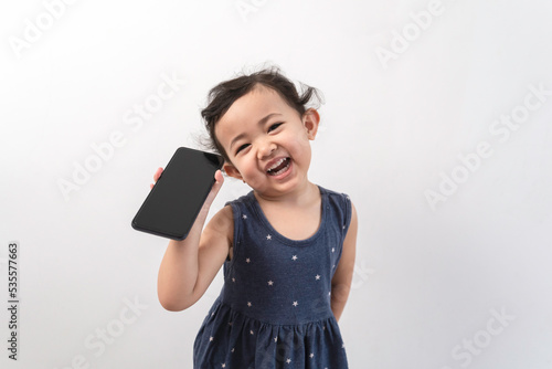 Smiling little asian girl kid showing blank screen of new popular mobile phone on white background. Excited Asian cute girl is using a smartphone, Phone empty screen display mockup.