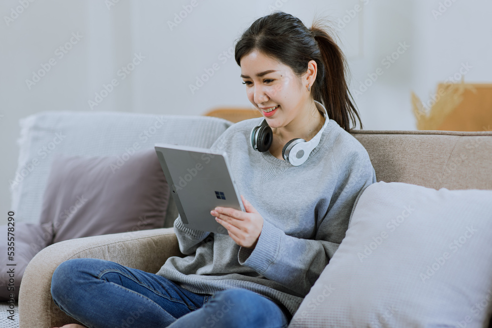 Happy Asian young woman using digital tablet technology sitting on the couch at home. Happy Asian young woman using digital tablet technology sitting on the couch at home.