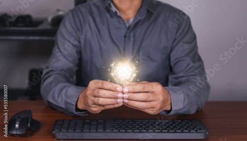 The hand of a man with a light bulb and he is using a notebook computer. Thinking differently creates inspiration and ideas. technologies can always come from creative and different ideas.