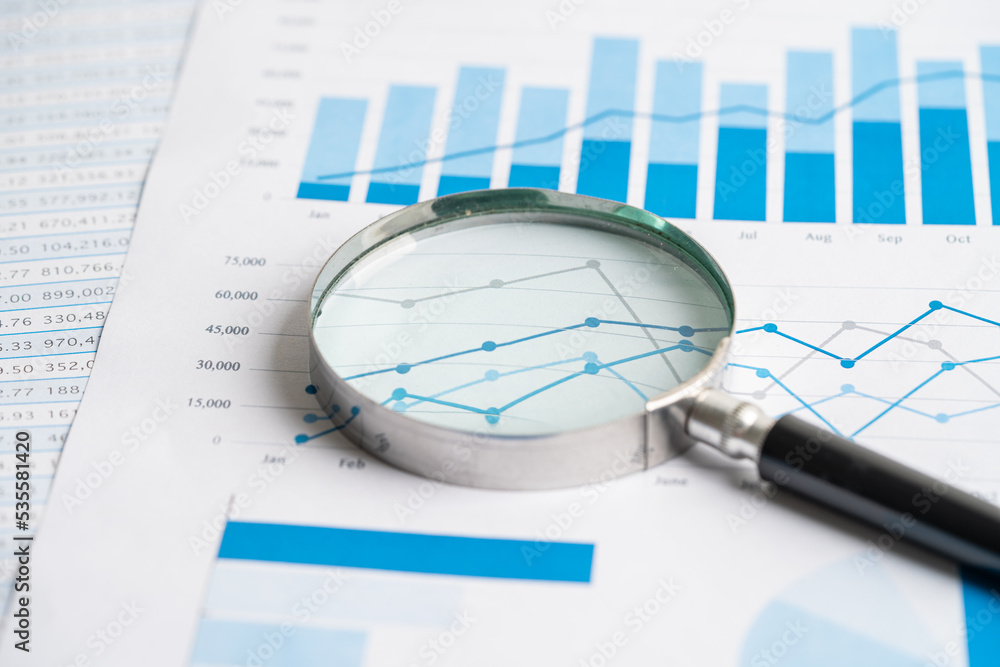 Magnifying glass on chart graph spreadsheet paper. Financial development, Banking Account, Statistics, economy, Stock exchange trading, Business office company meeting concept. Magnifying glass on chart graph spreadsheet paper. Financial development, Banking Account, Statistics, economy, Stock exchange trading, Business office company meeting concept.