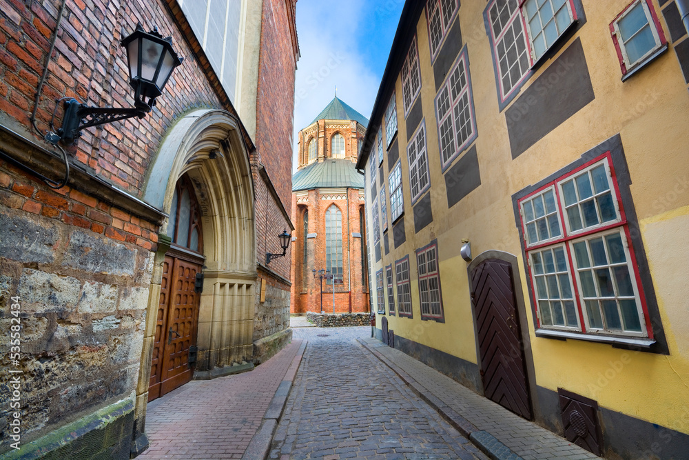 Narrow street by entrance portal of  St. John's Church in Riga, Latvia. St. Peter's Church in the background
