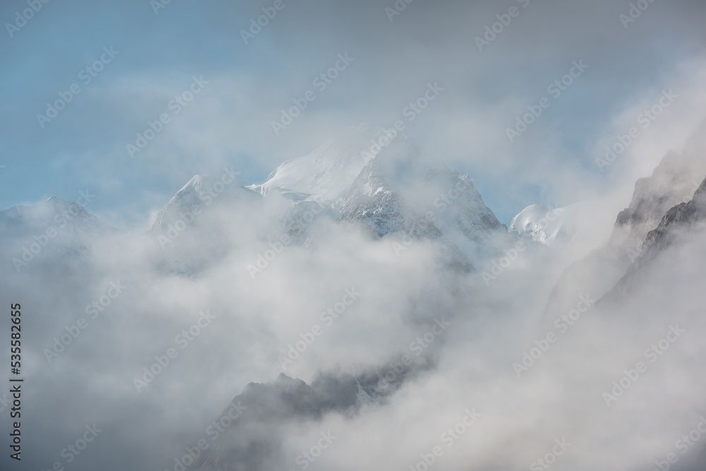 Beautiful snow castle in low clouds. Lovely scenery with high snowy mountains in thick clouds. Big air castles float in gantly cloudy sky. Scenic view to large snow mountain in clearance of dense fog.