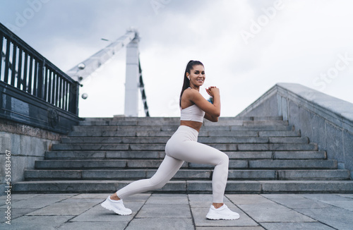 Young happy woman makes deep forward lunges to pump the muscles of the legs and buttocks, simple and effective exercises during morning jog around city. Healthy lifestyle and keeping the body in shape