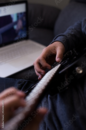 Young man learning to play guitar online with his laptop and guitar. Concept of virtual education and music. © artrolopzimages
