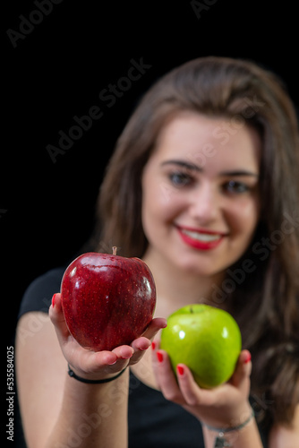 Szczęśliwa uśmiechnięta młoda dziewczyna proponuje zielone i czerwone jabłko
