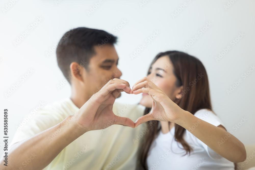 Couple or 2 asian people in bedroom, home or house. Man and woman to gesture hand in heart shape together. Look happy, romantic. Concept for married, family. Concept for love, valentine, relationship.