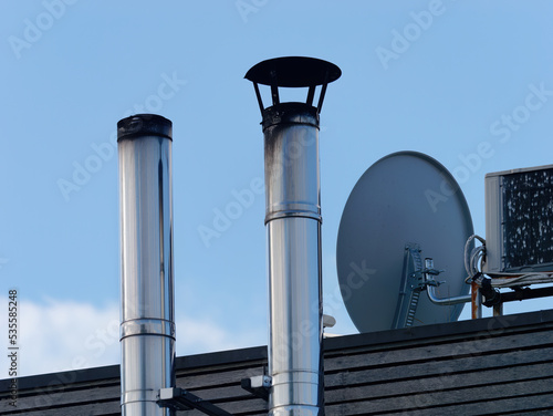 Close-up shot of two small metal chimneys on a wooden roof with a satellite dish