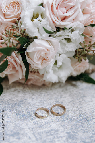 Golden wedding rings and a bridal bouquet of roses. Wedding details. Close-up