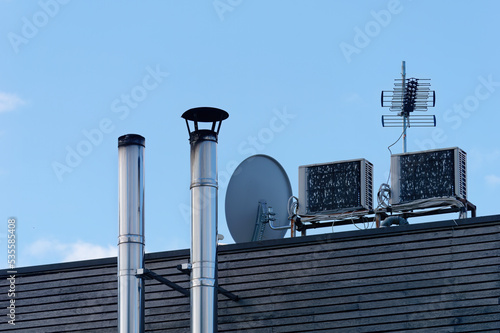 Close-up shot of two small metal chimneys on a wooden roof with an antenna and satellite dish