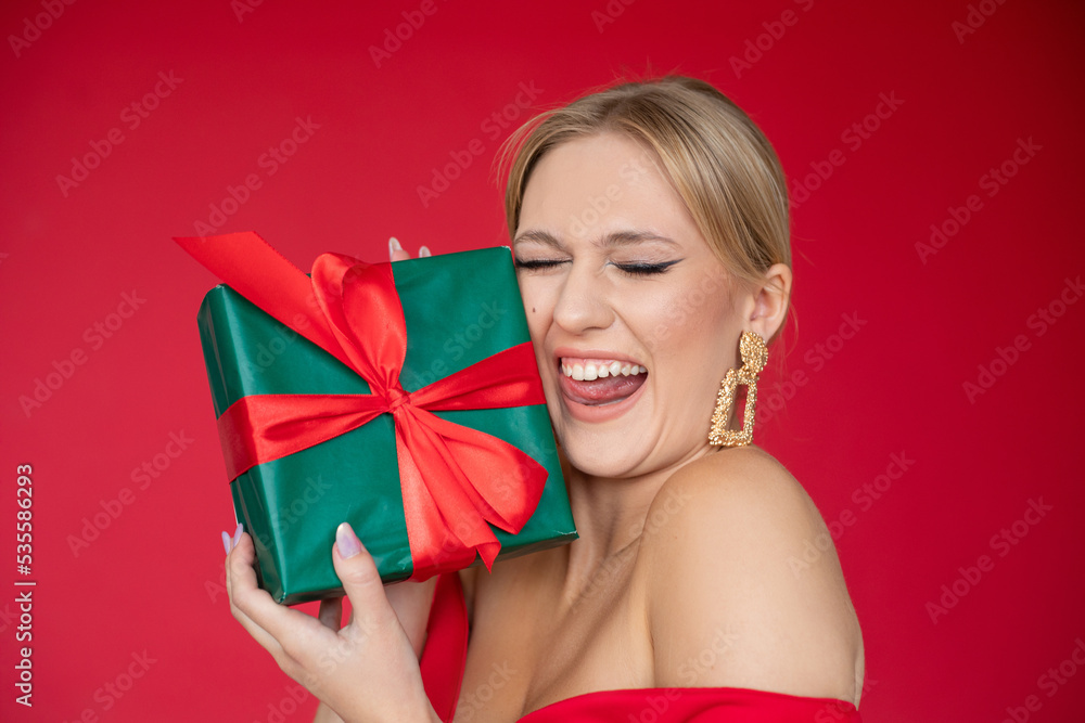 Happy cheerful woman in elegant red dress with evening makeup and hairstyle enjoy gift by closed eyes, red background. Present box, holiday celebration, birthday party, new year, christmas Happy cheerful woman in elegant red dress with evening makeup and hairstyle enjoy gift by closed eyes, red background. Present box, holiday celebration, birthday party, new year, christmas