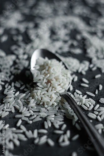 White rice scattered on the table and a small spoon, black background