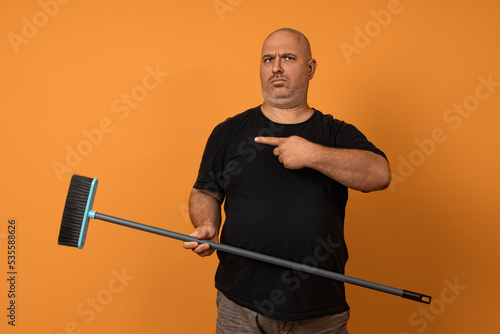 an adult man with a serious face and a mop in his hands points his finger to the left. concept get you there