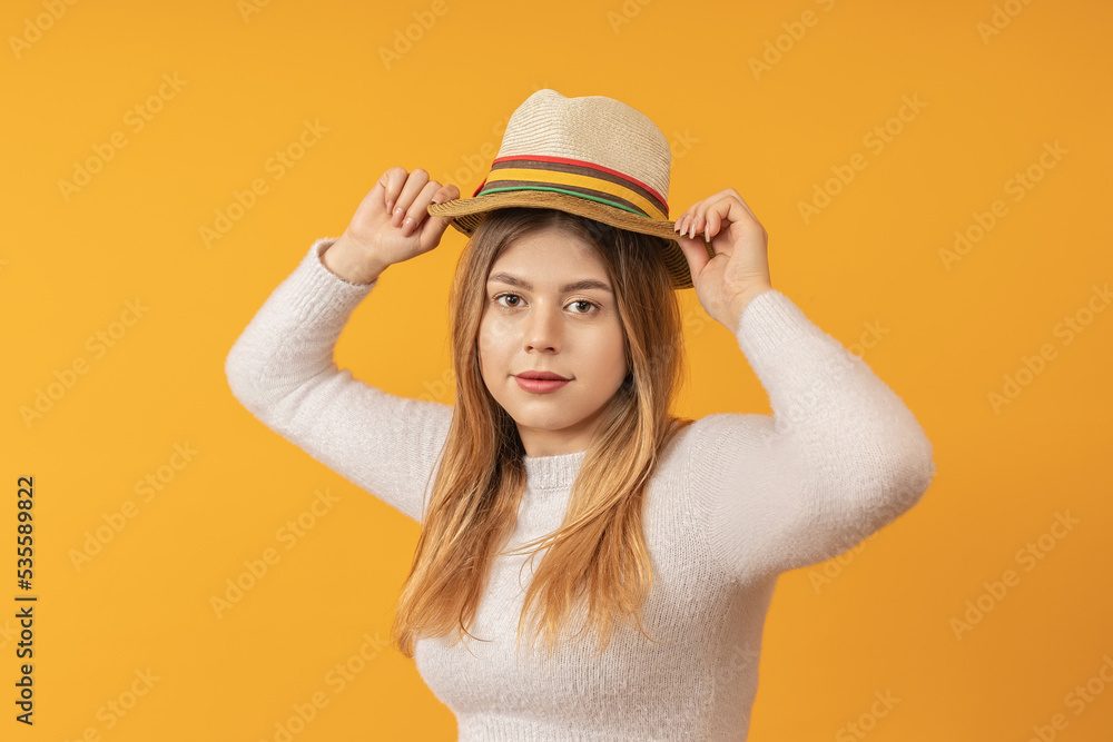 young beautiful elegant girl straightens her hat on her head with both hands, stands against a yellow background. travel concept young beautiful elegant girl straightens her hat on her head with both hands, stands against a yellow background. travel concept