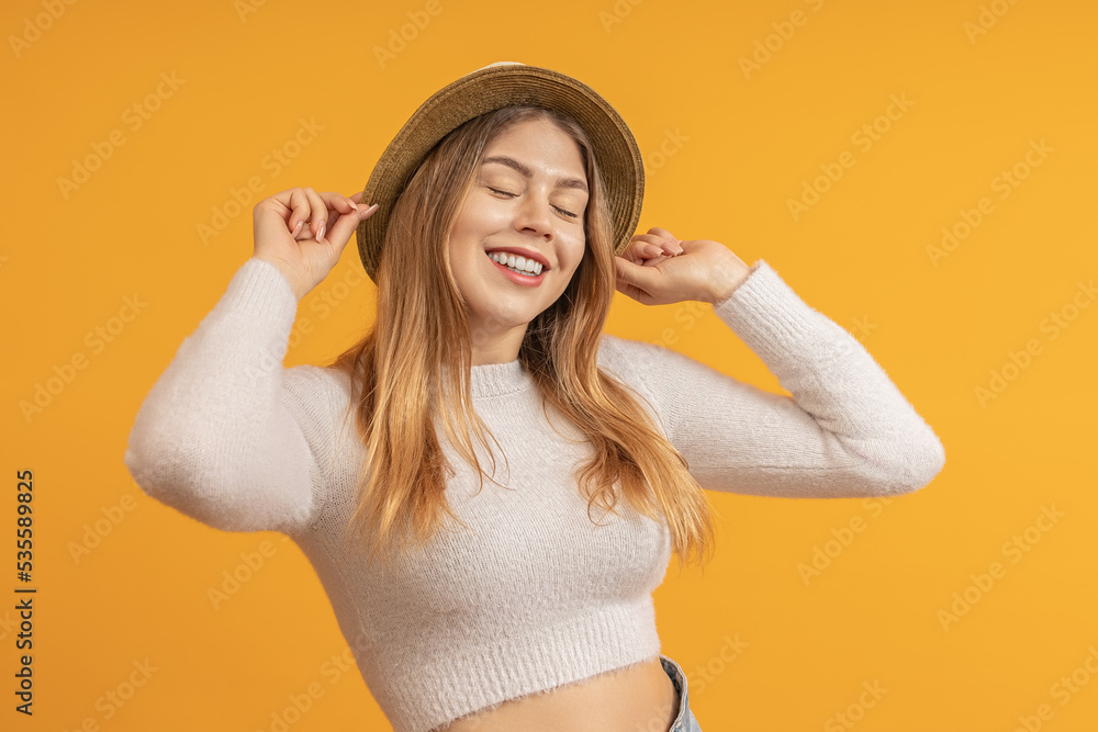 a young woman tries on a hat, smiles broadly and closes her eyes from happiness. colored background a young woman tries on a hat, smiles broadly and closes her eyes from happiness. colored background