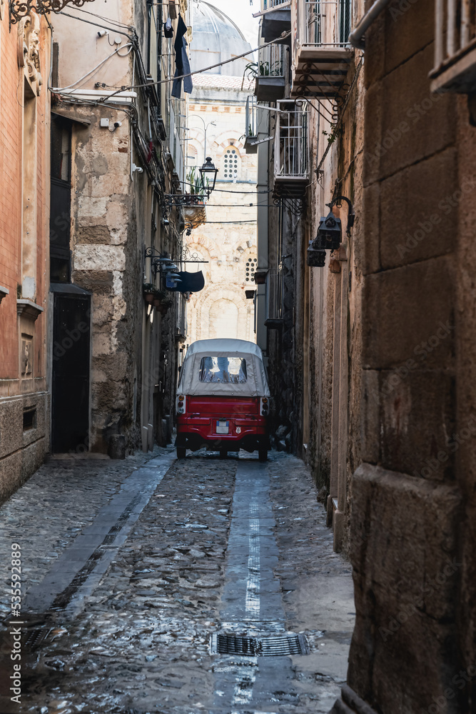 Old Piaggio Ape driving down a narrow street in the center of the old town of Tropea. Vintage car for transportation and tourist attraction. Travel vacation in Calabria, Southern Italy.