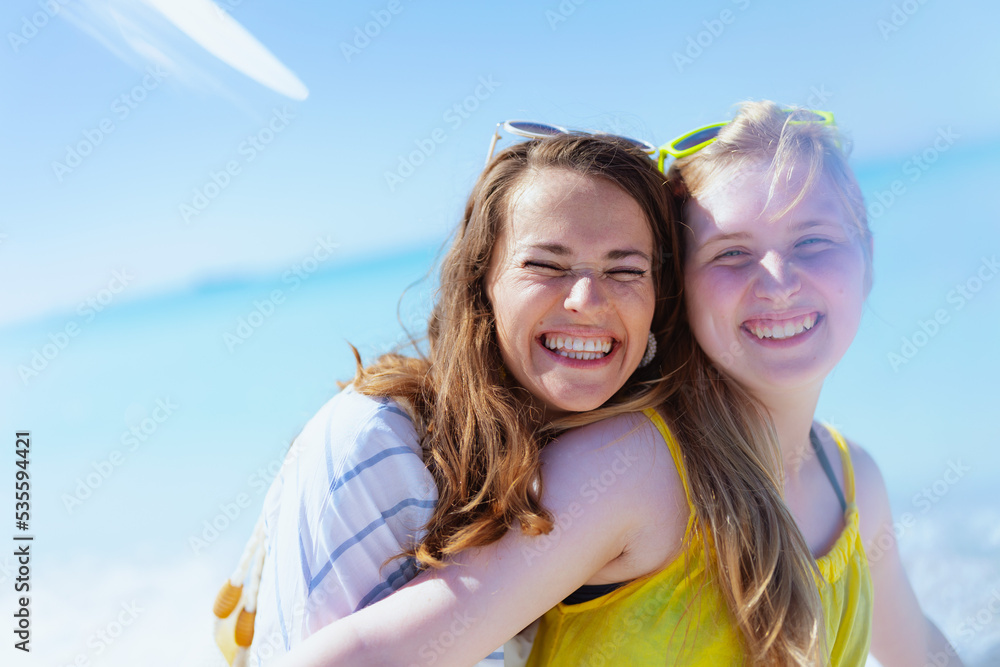 smiling stylish mother and teenage daughter at beach hugging