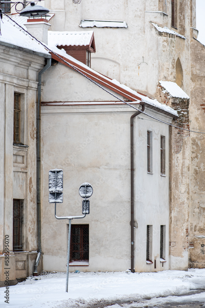Beautiful narrow street in Vilnius Old Town with old buildings and street signs in winter covered by the snow, vertical Beautiful narrow street in Vilnius Old Town with old buildings and street signs in winter covered by the snow, vertical
