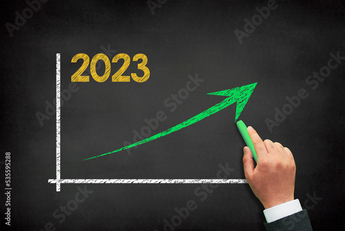 2023 chart arrow up for business with a male hand writing on chalkboard