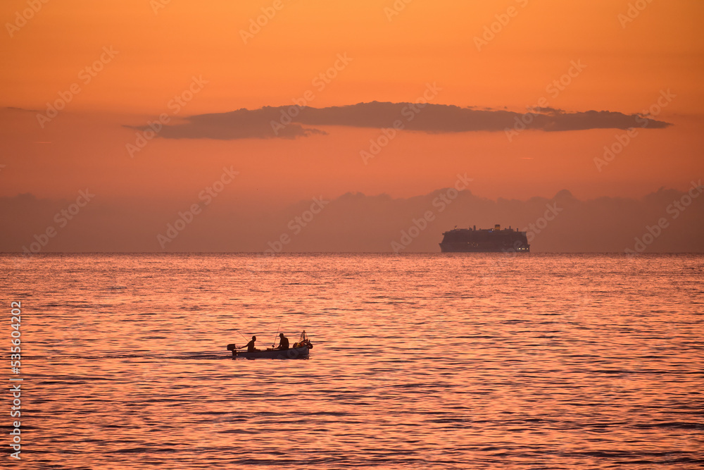 Silhouette of a boat with fishermen at sea in front of a beautiful sunrise. Ligurian Sea, Italy Silhouette of a boat with fishermen at sea in front of a beautiful sunrise. Ligurian Sea, Italy