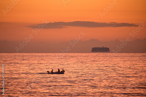 Silhouette of a boat with fishermen at sea in front of a beautiful sunrise. Ligurian Sea, Italy