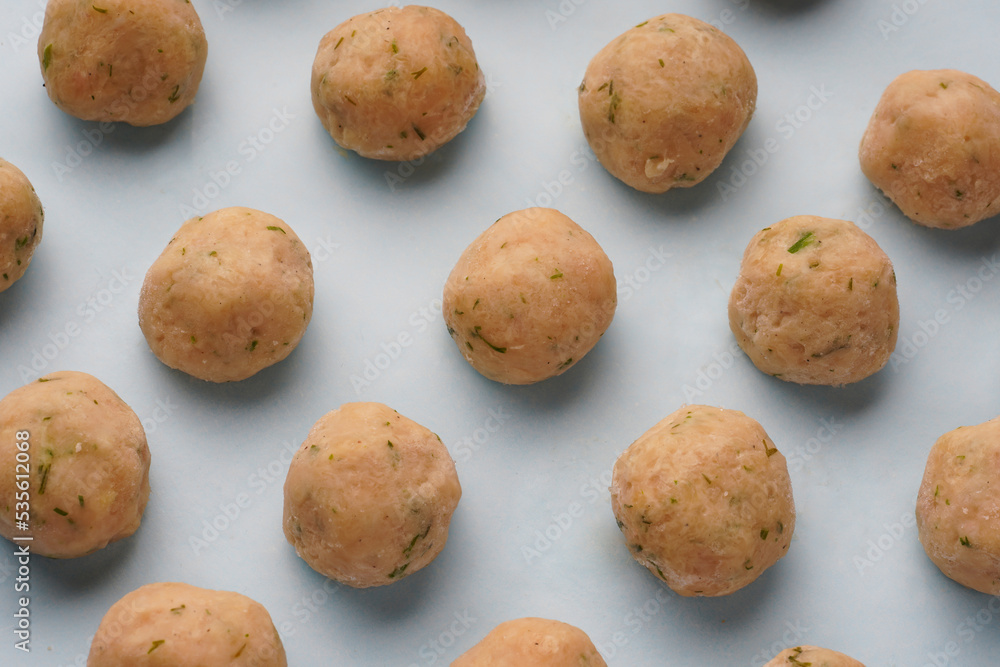 Fototapeta premium Small raw frozen meatballs of light meat on a blue background. Semi-finished products for homemade meatballs and soup