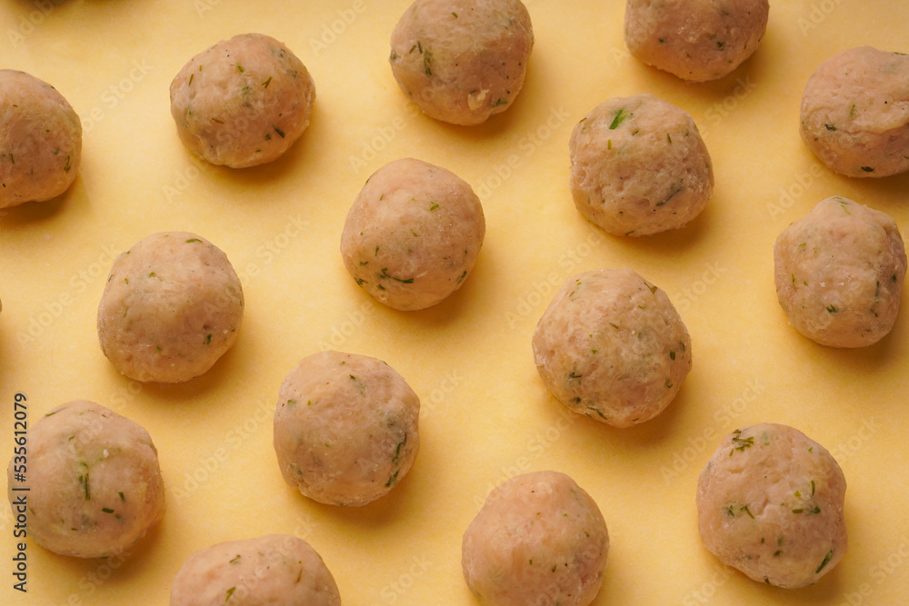 Fototapeta premium Close-up of frozen meatballs on a yellow background. Semi-finished products for homemade meatballs from chicken with spices.