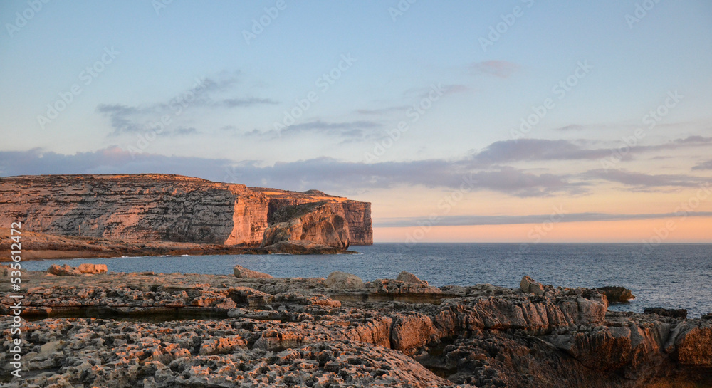Sunset over the sea and the famous cliffs of The Stone Crocodile and Fungus Rock, on the island of Gozo, Malta