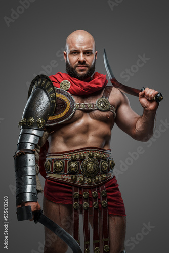 Shot of roman gladiator from ancient rome dressed in armor and cloak against gray background.