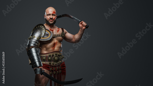 Studio shot of powerful gladiator from past dressed in armor holding dual swords.
