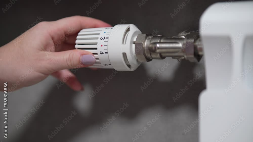 Hand adjusting temperature on heating radiator thermostat, saving energy by adjusting heating thermostat. Hand adjusting temperature on heating radiator thermostat, saving energy by adjusting heating thermostat.