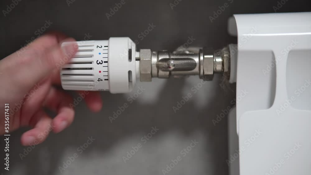 Hand adjusting temperature on heating radiator thermostat, saving energy by adjusting heating thermostat. Hand adjusting temperature on heating radiator thermostat, saving energy by adjusting heating thermostat.