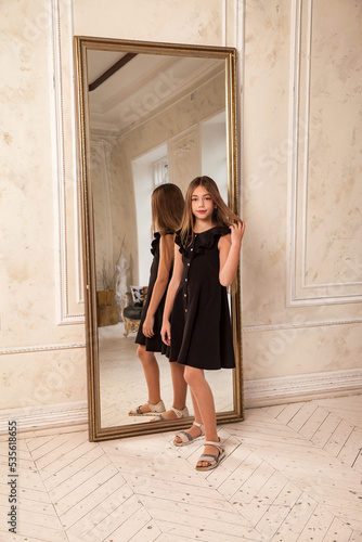 Teenager girl princess 10 year old portrait with curly hair, posing looking at camera, fashion model in stylish black elegant dress in living room. Fashionable young lady actress. Copy text space