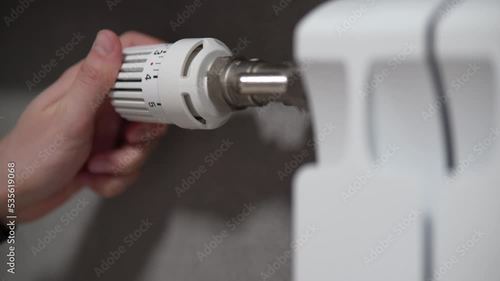 Hand adjusting temperature on heating radiator thermostat, saving energy by adjusting heating thermostat. Hand adjusting temperature on heating radiator thermostat, saving energy by adjusting heating thermostat.
