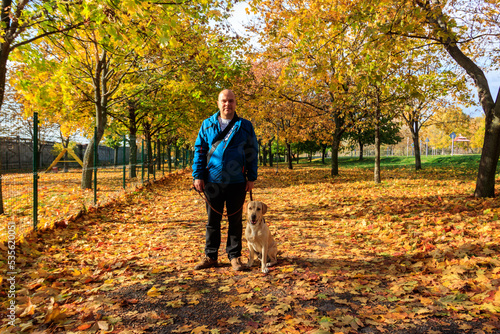 Handsome man walking his labrador retriever dog in autumn park