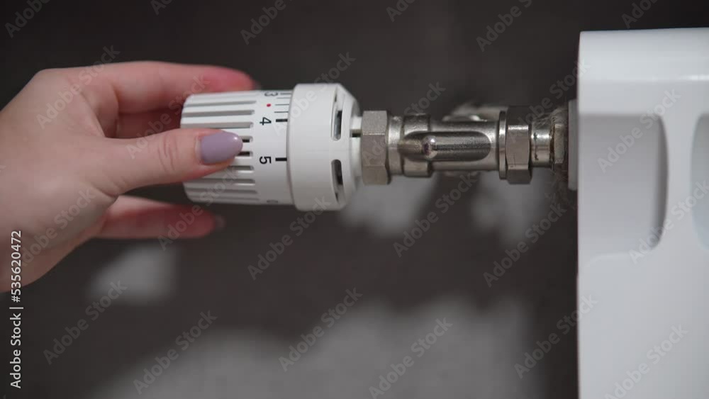 Hand adjusting temperature on heating radiator thermostat, saving energy by adjusting heating thermostat. Hand adjusting temperature on heating radiator thermostat, saving energy by adjusting heating thermostat.