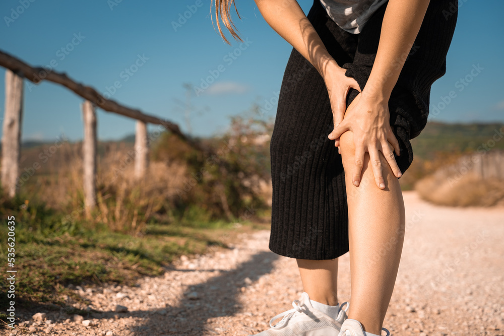 Girl massaging his knees after running in the hills. She had knee pain and could not walk. Need to be treated. Health problem and people concept. Sport traumas concept. Close up legs. Unrecognizable c