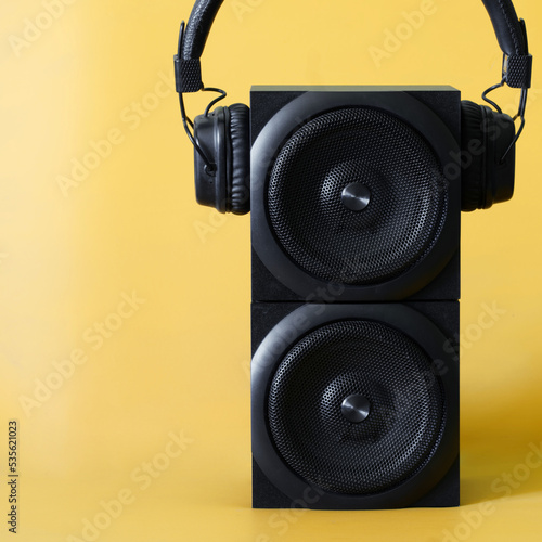 Vertical black two-way audio speaker and wireless headphones with ear pads on a yellow background. Concept of pop music, audio podcasts and broadcast. Copy space photo