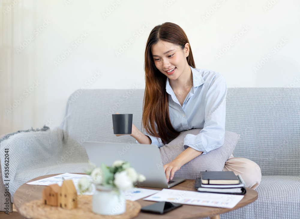 Female freelance is typing information on laptop and drinking coffee while sitting on comfortable Female freelance is typing information on laptop and drinking coffee while sitting on comfortable