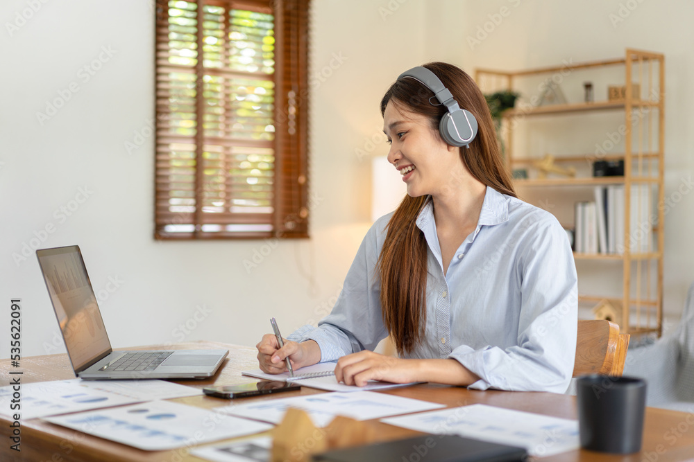 Female freelance is reading business data on laptop and writing information on notebook while wearing Female freelance is reading business data on laptop and writing information on notebook while wearing